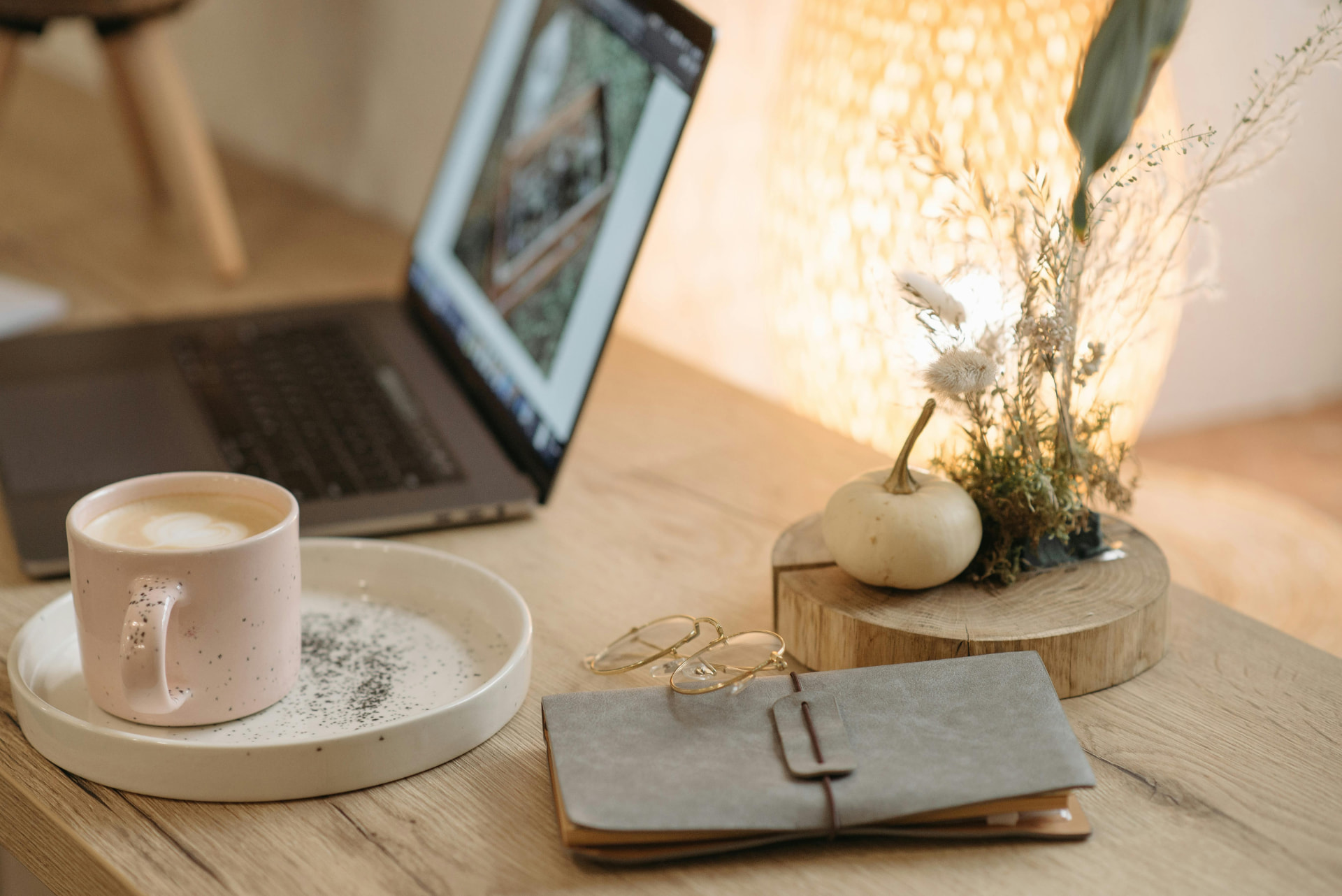 A warm desk with a latte, notebook and dried flowers by lamplight